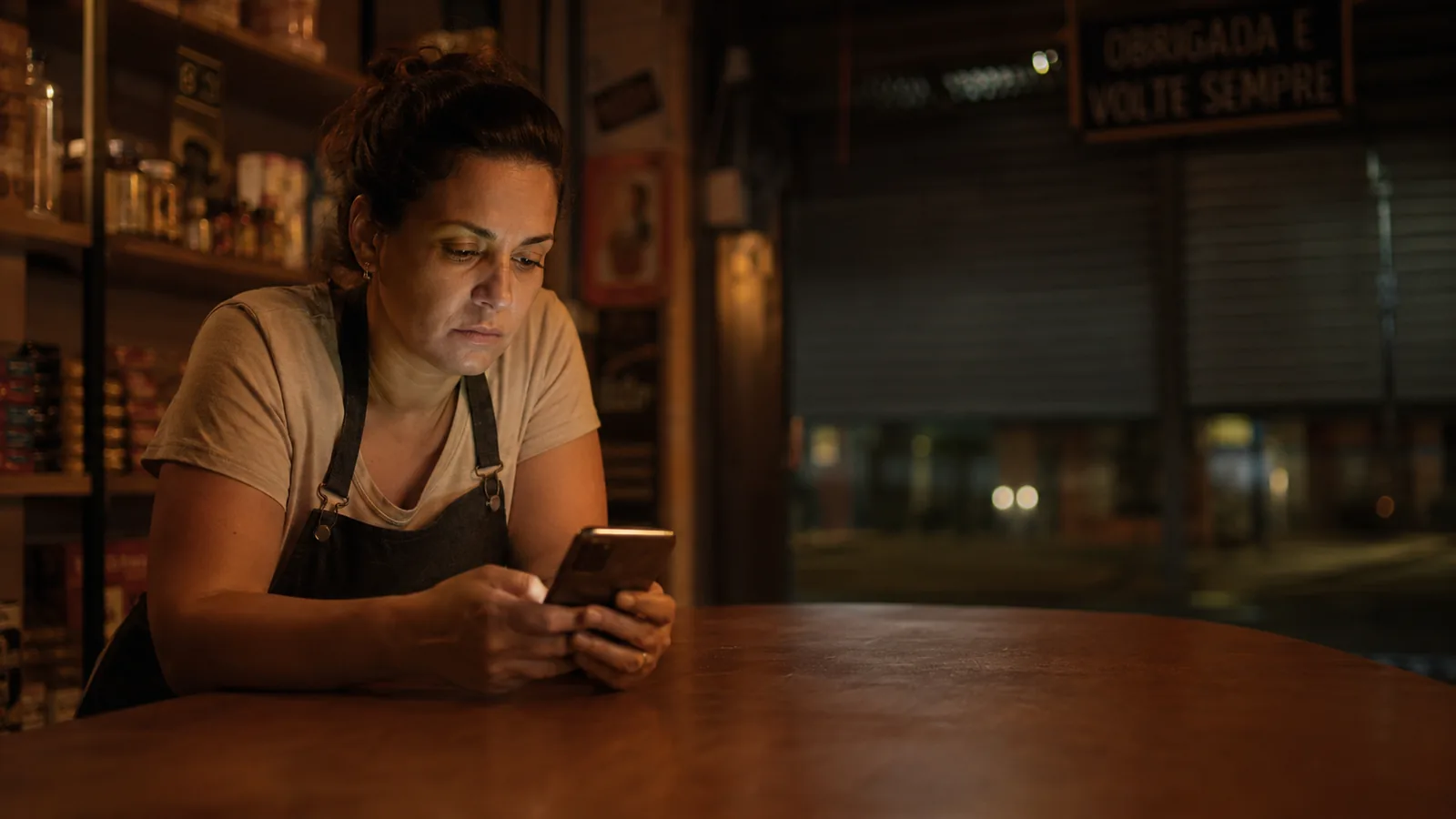 Dona de negócio local à noite, ainda no celular depois de um dia longo